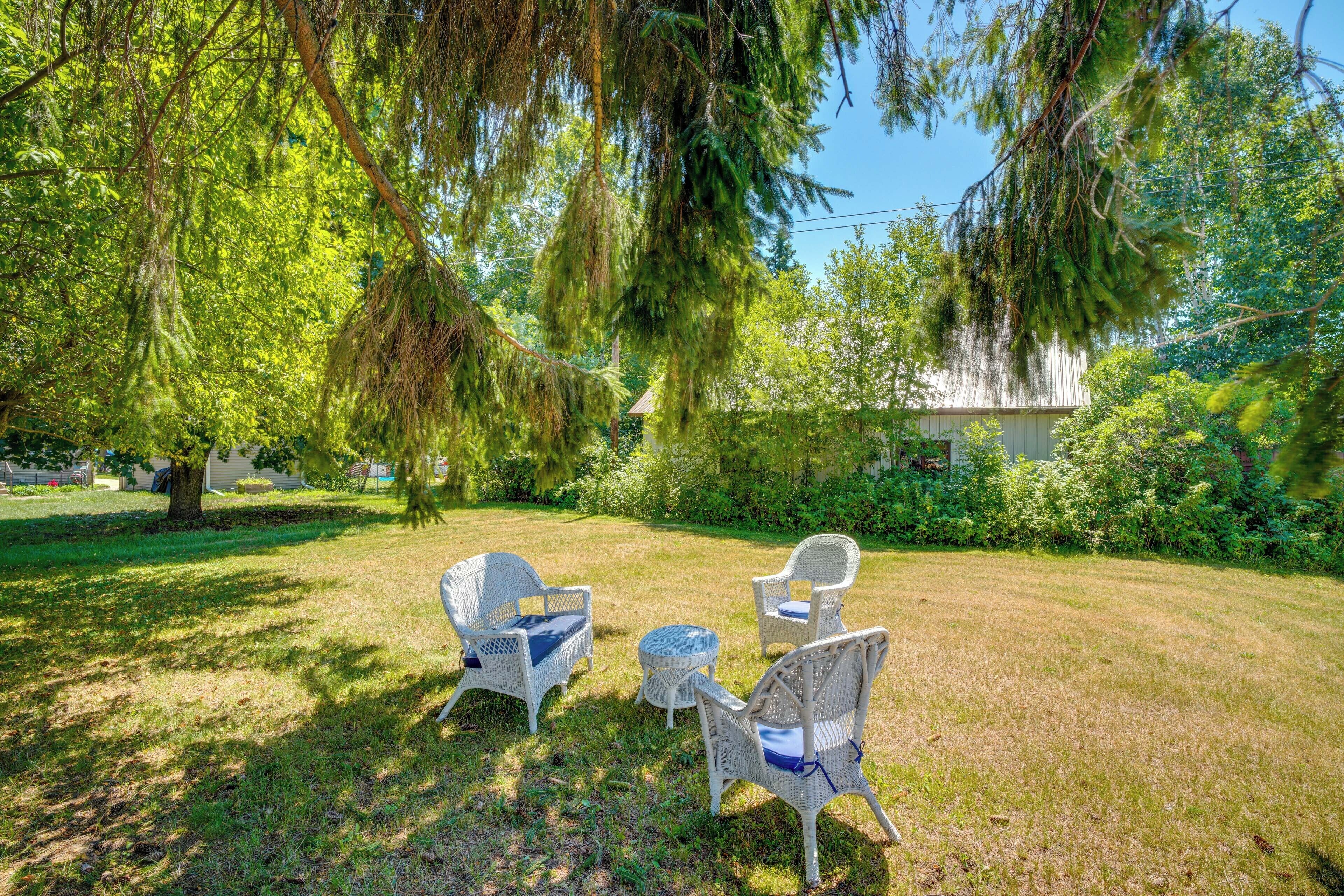 An outdoor seating area with wicker chairs and a small table, surrounded by grass and trees.