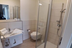 Een moderne badkamer met een douchecabine van glas, een witte wastafel en een toilet.