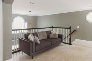 Ein Wohnzimmer mit einem dunkelbraunen Sofa, Fenstern mit weißen Rahmen und einer Treppe.