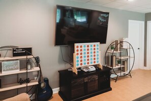 Un saló amb un televisor de pantalla plana fixat a la paret, una guitarra, una estant amb un cartell i un joc de taula.