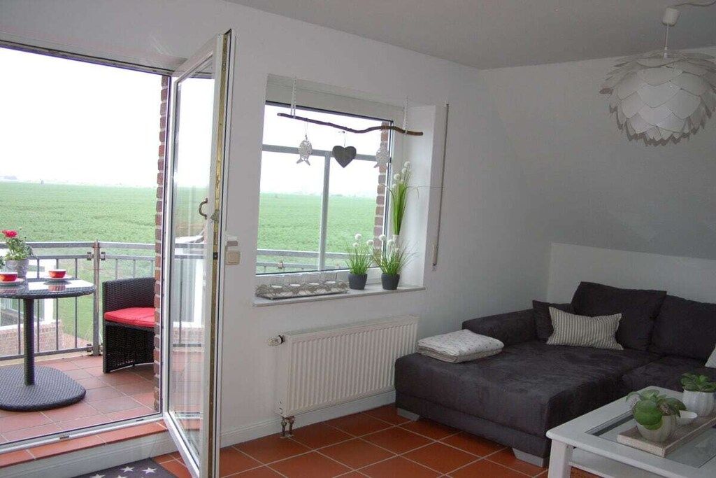 Ein Wohnzimmer mit einer Couch, einem Tisch, einem Fenster mit Blick und einem Balkon mit Gartenmöbeln.