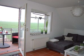 A living room with a sofa, a table, a window with a view, and a balcony with outdoor furniture. - Holiday apartment in Upleward with balcony (Upleward)