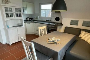 A compact kitchen with white cabinets, a dining table, and a sofa. - Holiday apartment in Upleward with balcony (Upleward)
