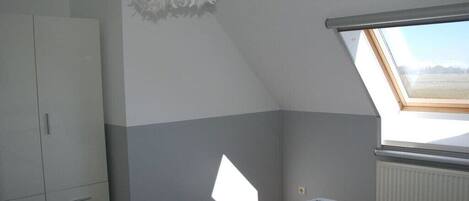 A bedroom with a skylight, a wardrobe, and a bed with a patterned bedspread.