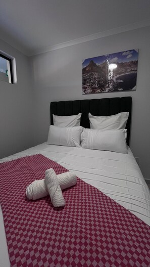 A hotel room with a bed, a red and white checkered blanket, white pillows, and a framed picture of a mountain landscape on the wall. - Tranquil 1-bedroom Apartment in Roodepoort, South Africa (Johannesburg)