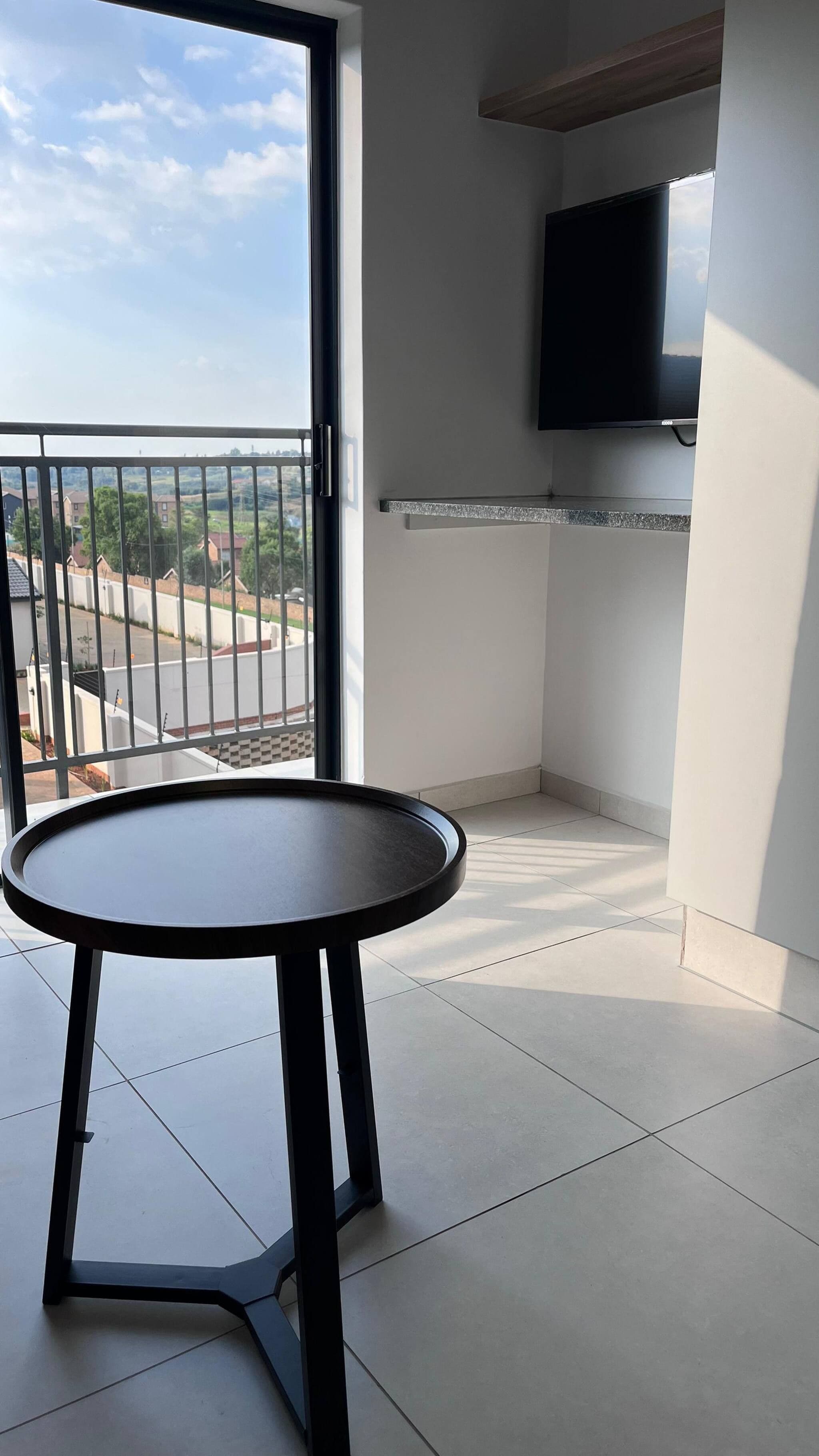 Ein Balkon mit einem runden Tisch, einem an der Wand befestigten Fernseher und Blick ins Freie.