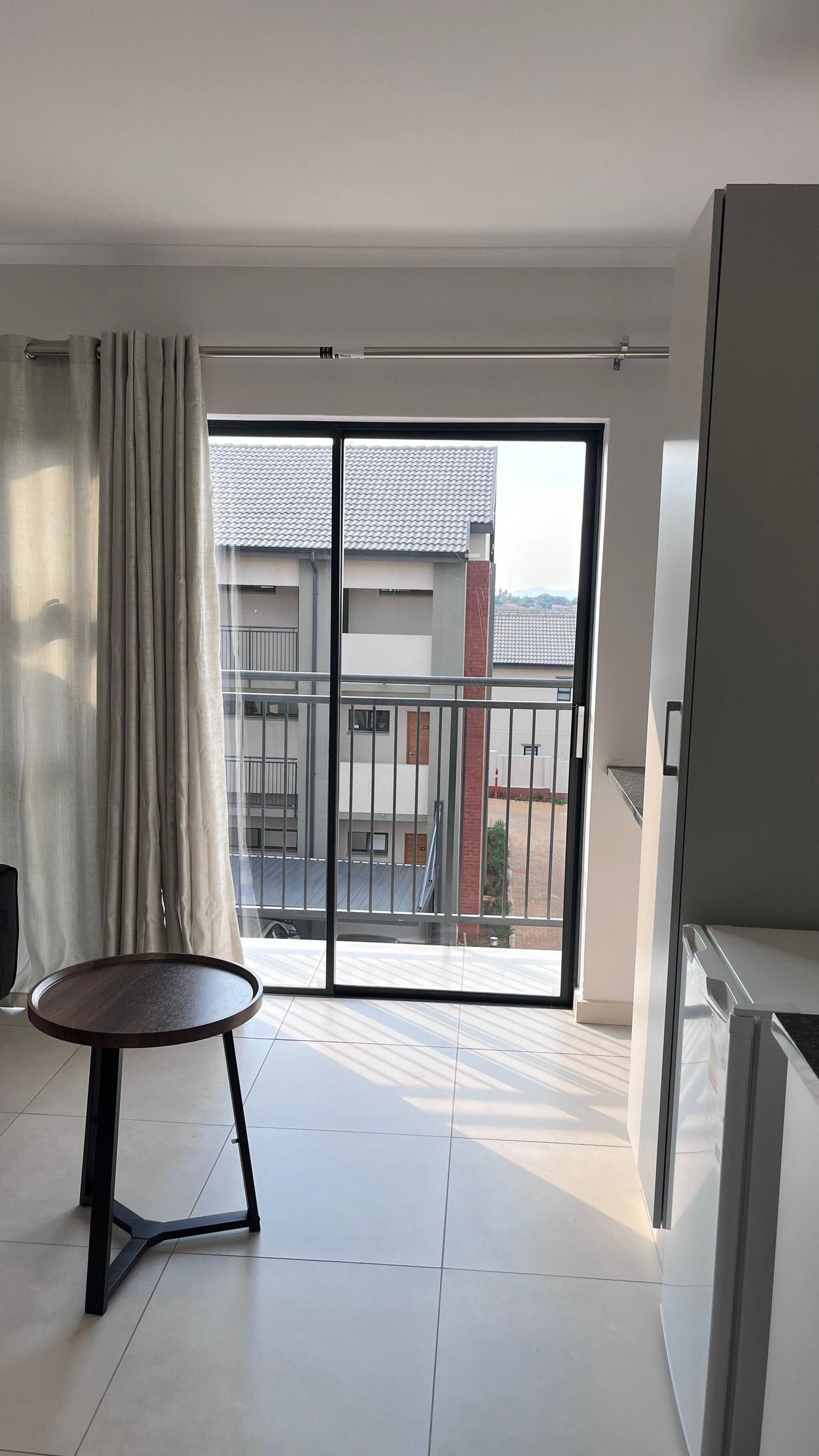 A modern apartment with a balcony, a round table, and a sliding glass door.