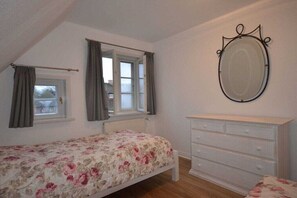 A bedroom with a bed, a dresser, a window with curtains, and a wall-mounted mirror. - Holiday home with 3 bedrooms (Süderende)