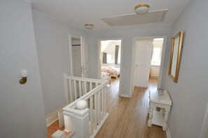 A hallway with a white railing, a small table, and a door leading to a bedroom with a bed. - Holiday home with 3 bedrooms (Süderende)
