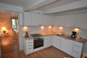 A modern kitchen with white cabinets, a built-in oven, a sink, and a countertop with a coffee maker. - Holiday home with 3 bedrooms (Süderende)