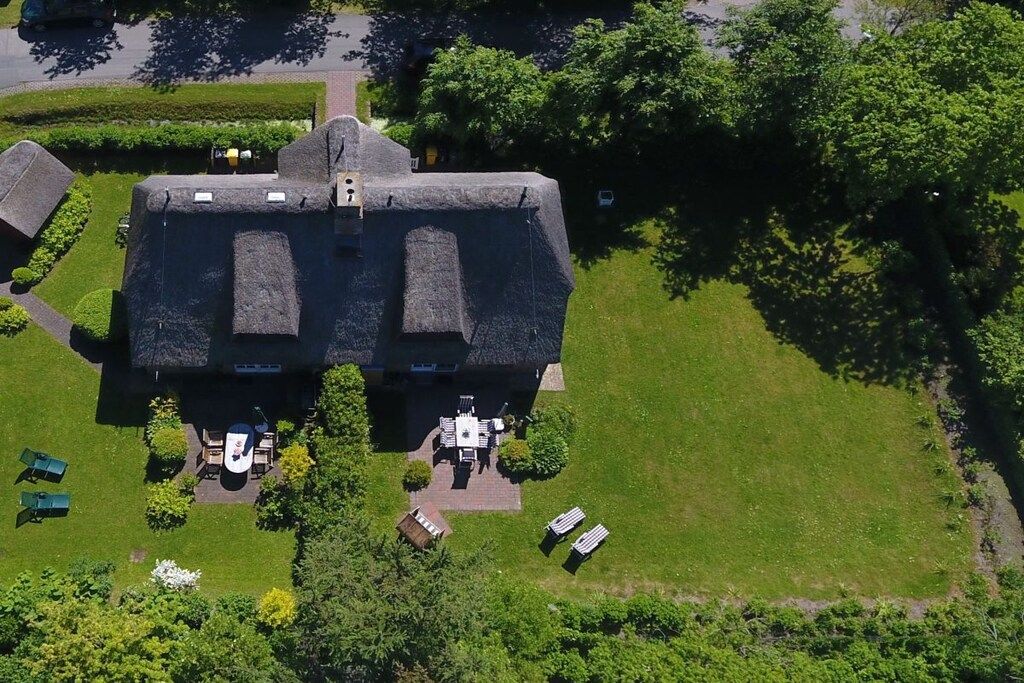 A large house with a symmetrical roof, surrounded by a well-maintained lawn and trees.