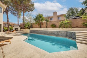 Ein Swimmingpool mit gefliesten Rändern, umgeben von Liegestühlen und einer Terrassenfläche.