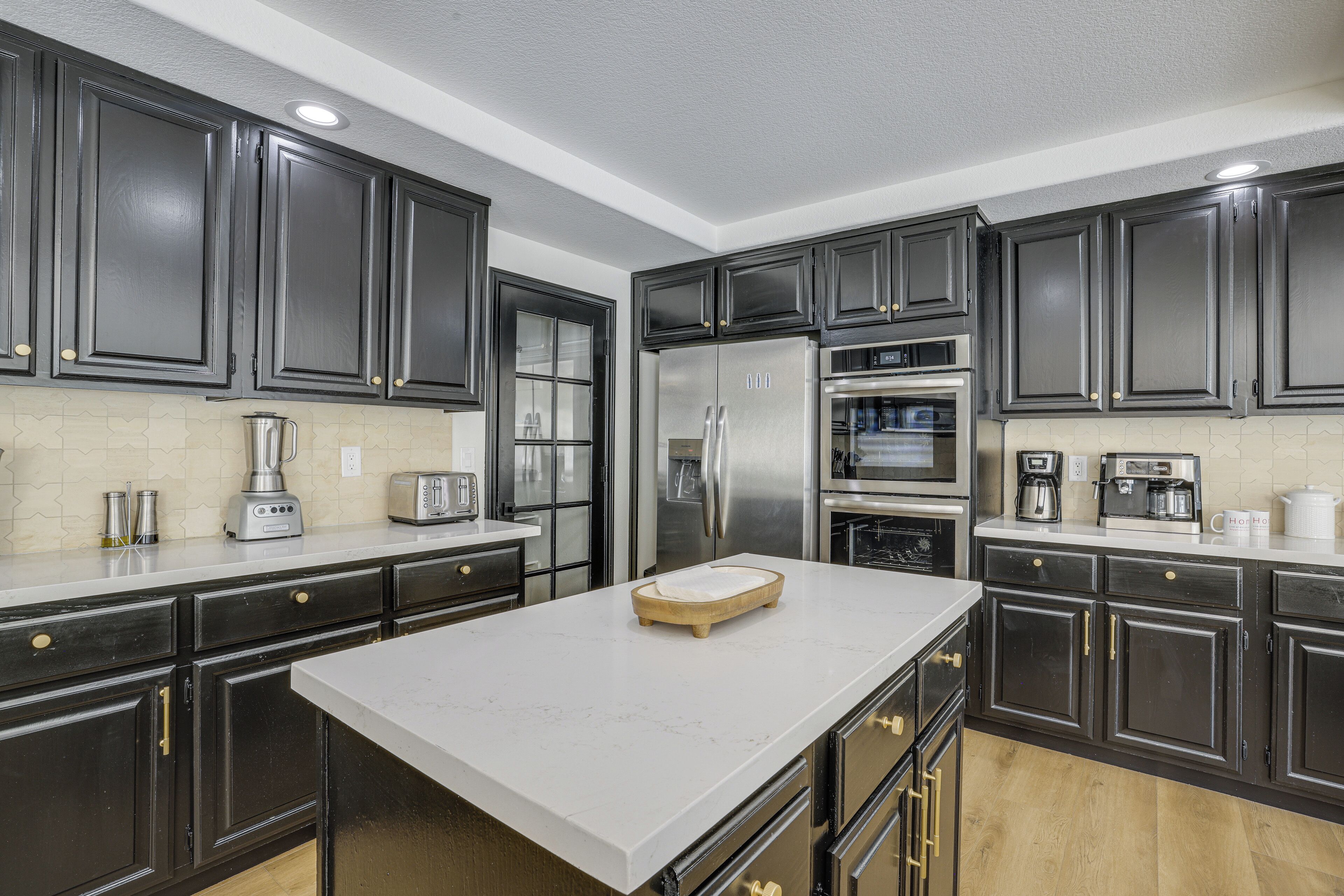 A modern kitchen with dark cabinetry, stainless steel appliances, and a marble countertop.