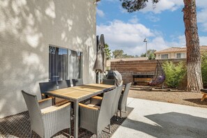 Eine Terrassenanlage im Freien mit Tisch, Stühlen, einem Grill und einer Pergola.