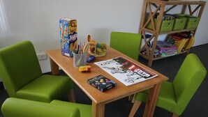 A room with a wooden table, green chairs, a bookshelf, and various board games. - Holiday home in Wingst with swimming pool (Wingst)