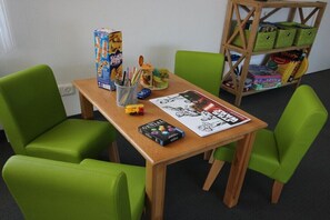 Une pièce avec une table en bois, des chaises vertes, une bibliothèque et divers jeux de société.