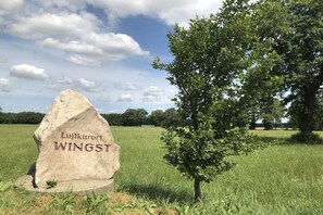 A stone marker with the inscription 'Luftkurort WINGST' in a grassy field with trees and a clear sky. - Holiday home in Wingst with swimming pool (Wingst)