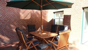 An outdoor patio with a wooden table and chairs, a large umbrella, and a brick wall. - Holiday home in Wingst with swimming pool (Wingst)