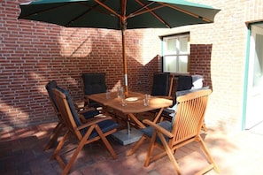 Une terrasse extérieure avec une table et des chaises en bois, un grand parasol et un mur en briques.
