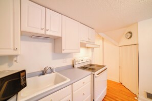 Una cucina con mobili bianchi, un fornello, un forno a microonde e un lavello.