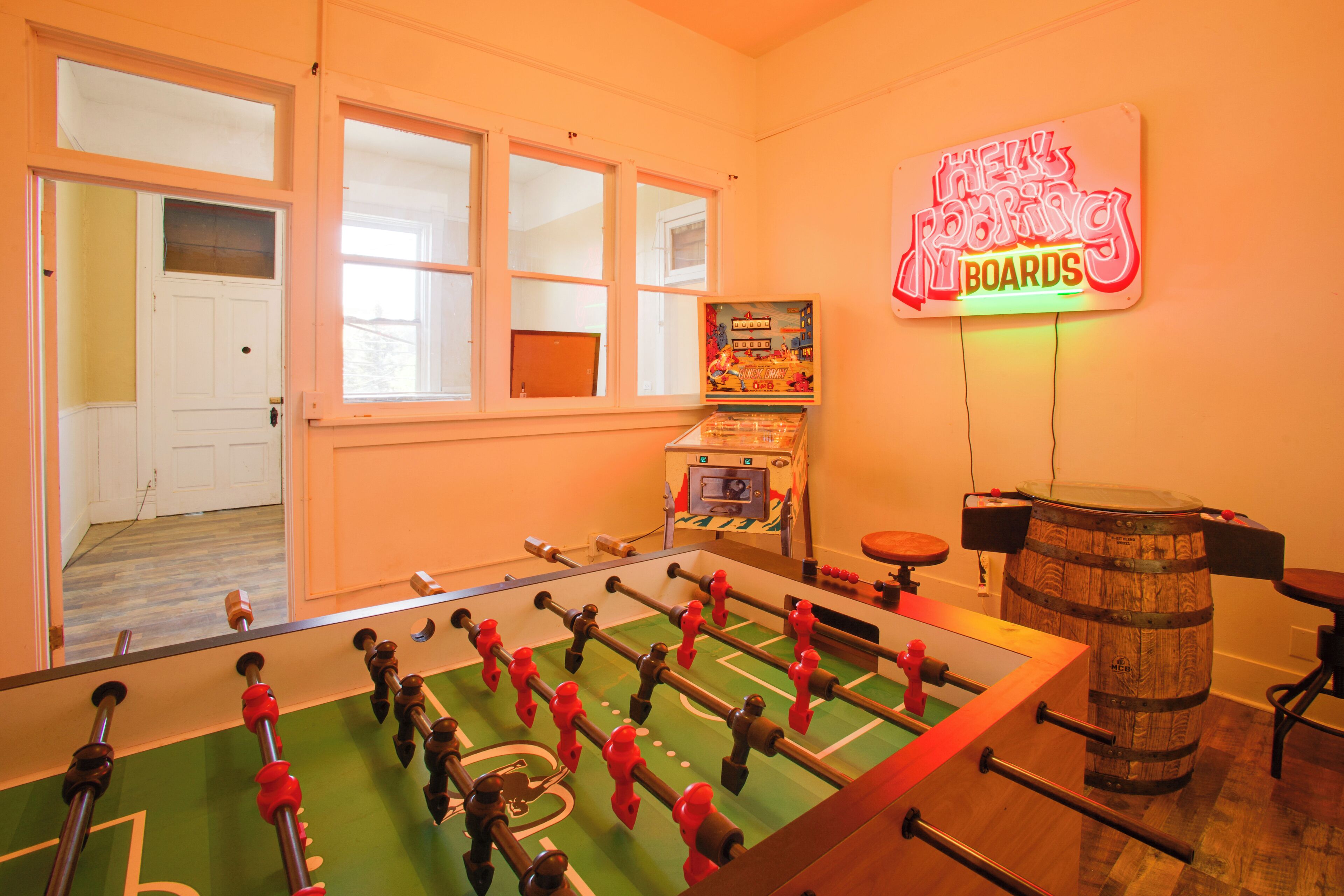 Een kamer met een tafelvoetbaltafel, een neonbord en een houten vat.