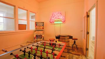 Una habitación con una mesa de fútbol de mesa, un letrero de neón y una ventana.