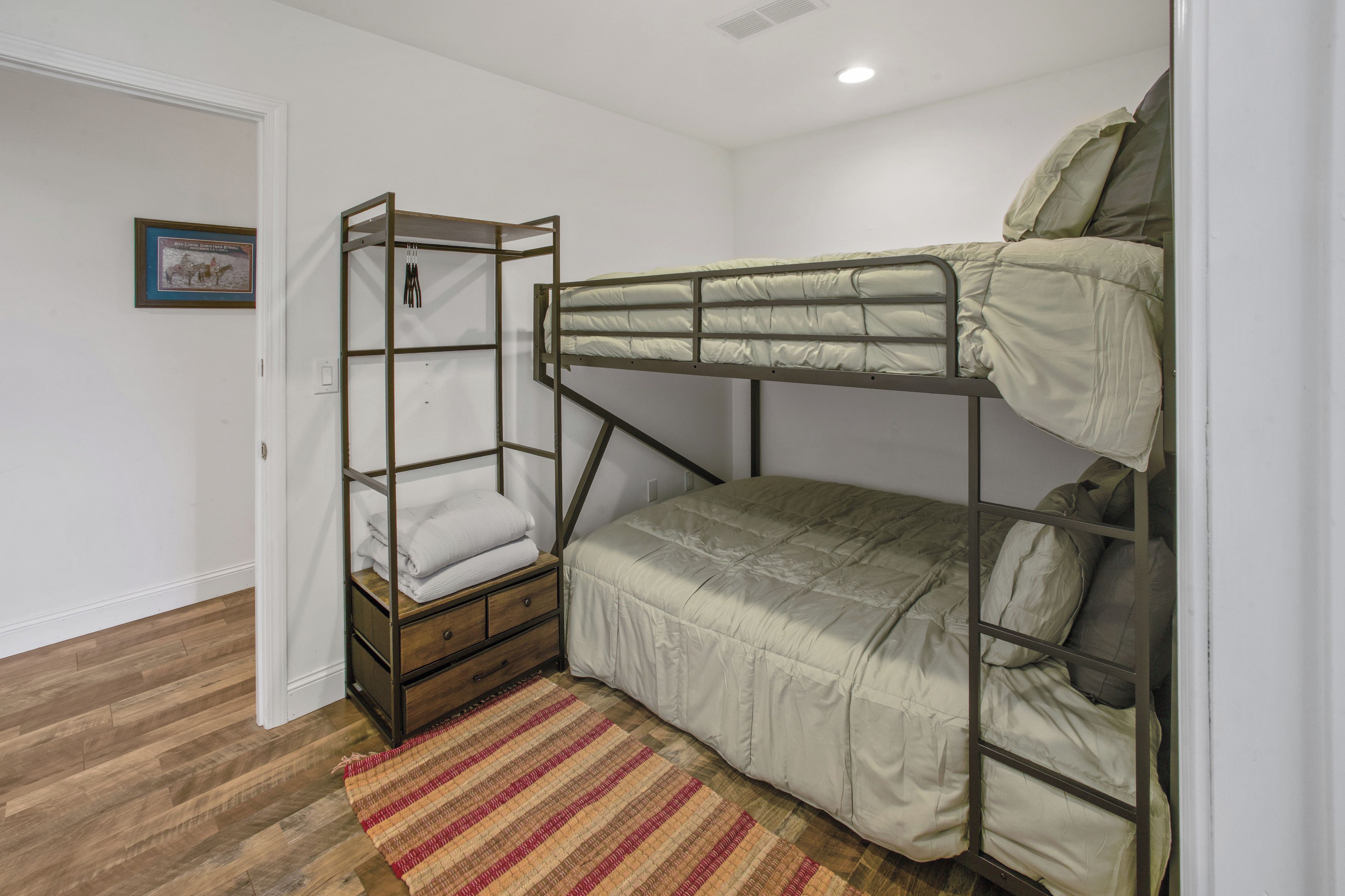 A bunk bed room with a wooden ladder, a small wooden cabinet, and a striped rug on the floor.