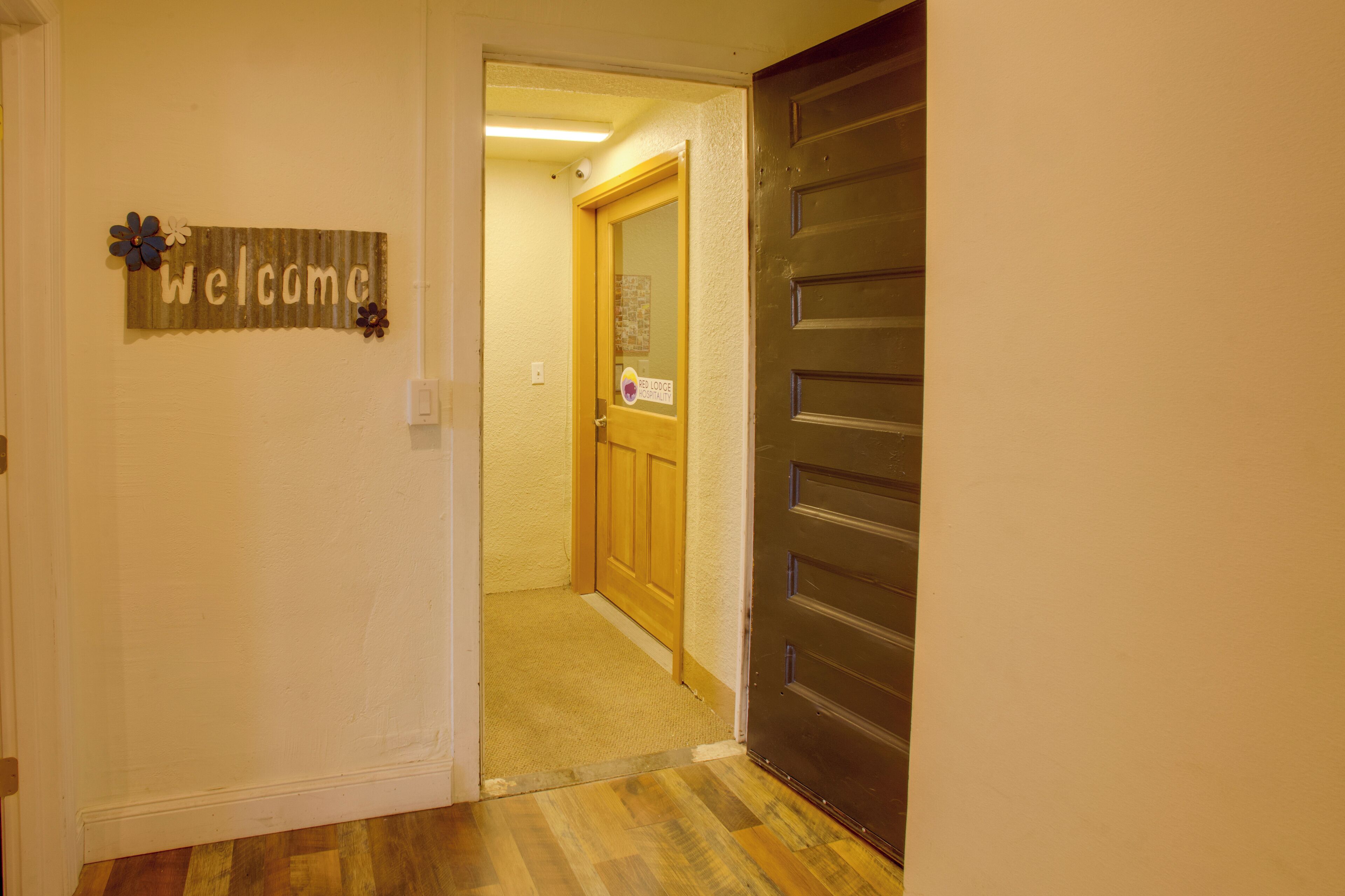 A hallway with a wooden door, a welcome sign, and a bulletin board.