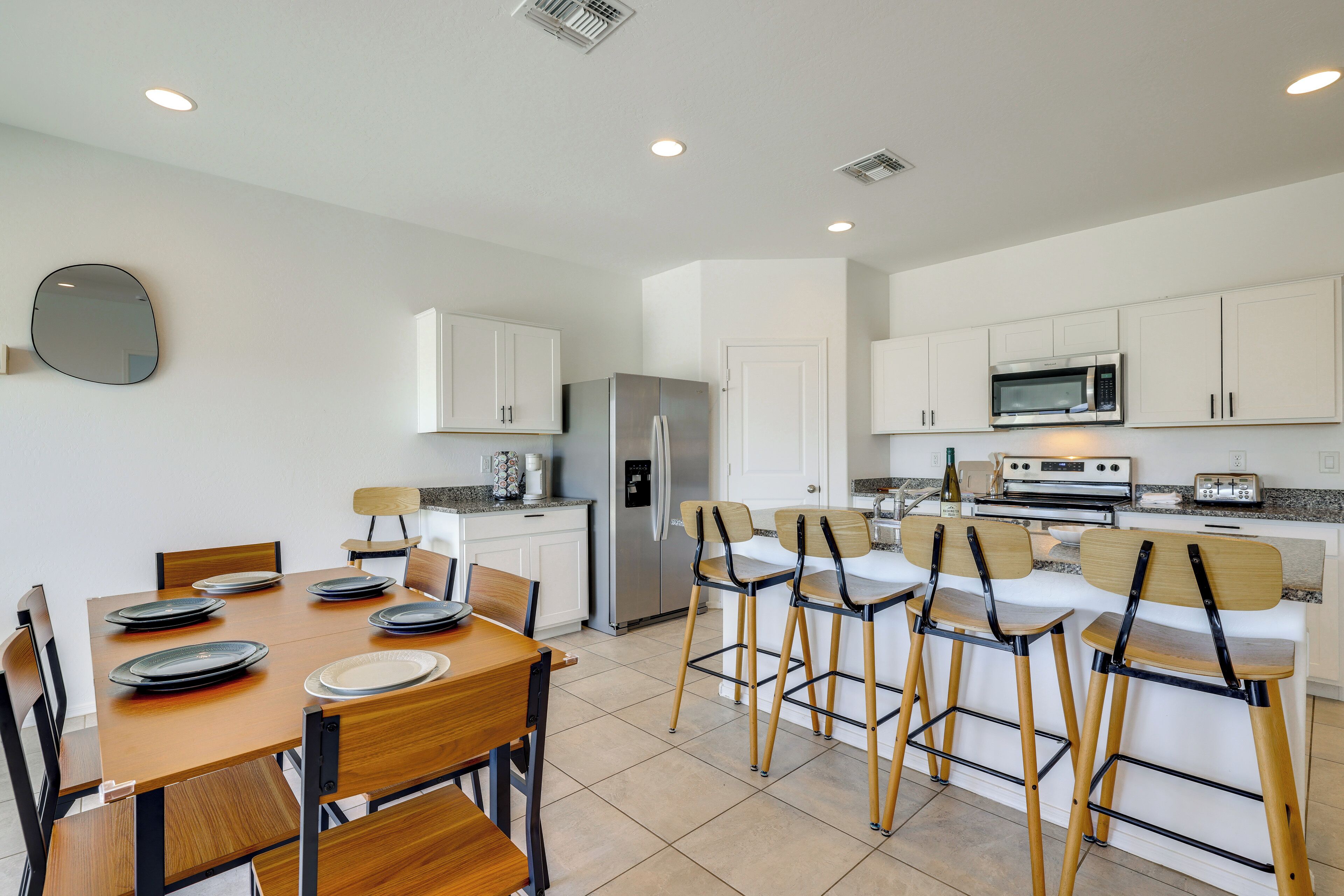 A modern kitchen with white cabinets, stainless steel appliances, and a dining area with wooden chairs and plates.