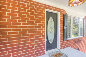 Casa de tijolos com porta preta, janela emoldurada por branco e tapete de entrada com a palavra 'HOME'.