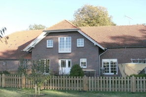 A two-story brick house with a sloped roof, a wooden fence, and a small tree in the front yard. - Holiday home with 2 bedrooms (Bockhorn\/Bredehorn)