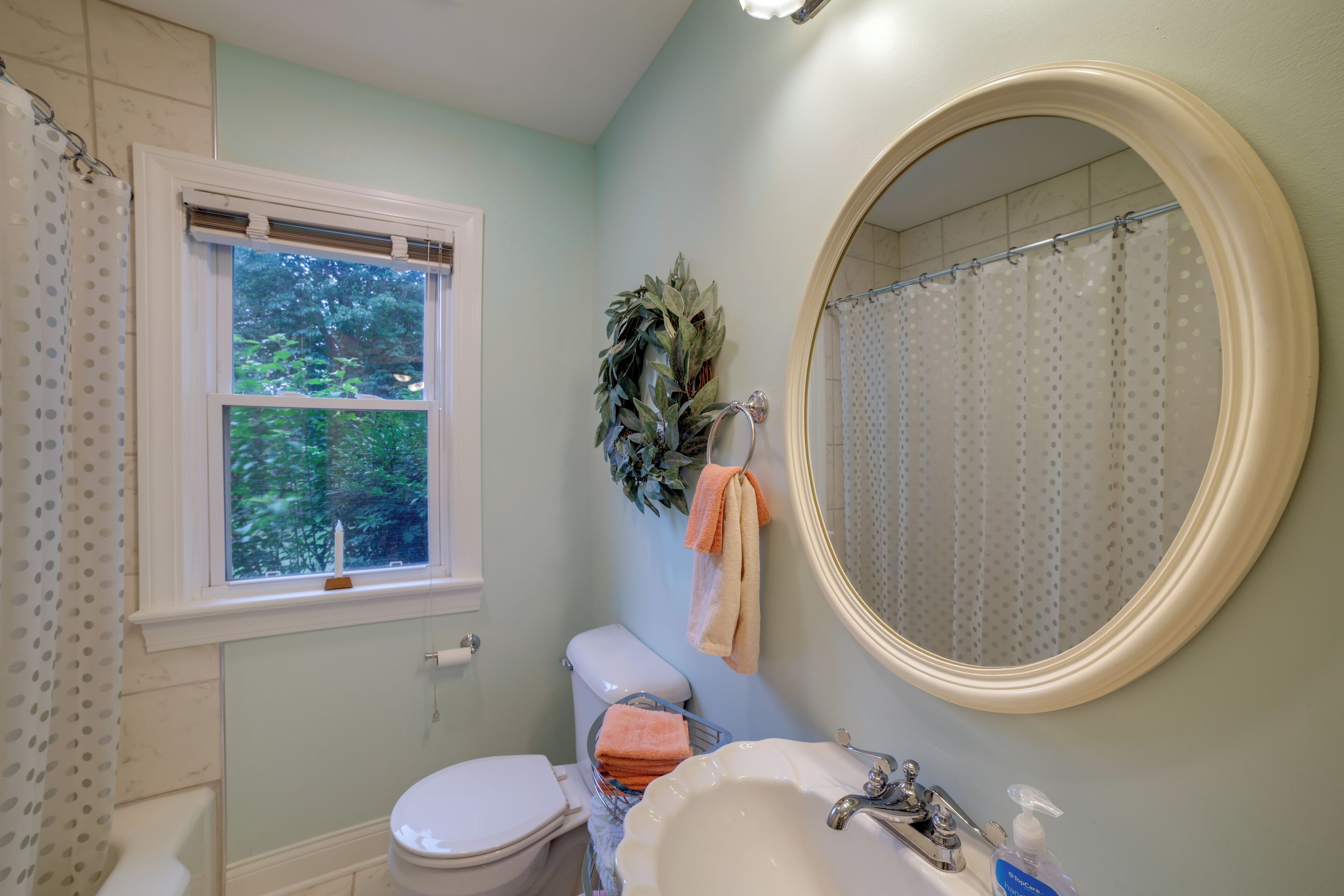 A bathroom with a toilet, sink, and a window with a view of trees.