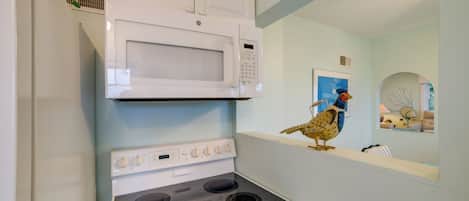 A kitchen with a white microwave, a stove, and a decorative bird on the wall.