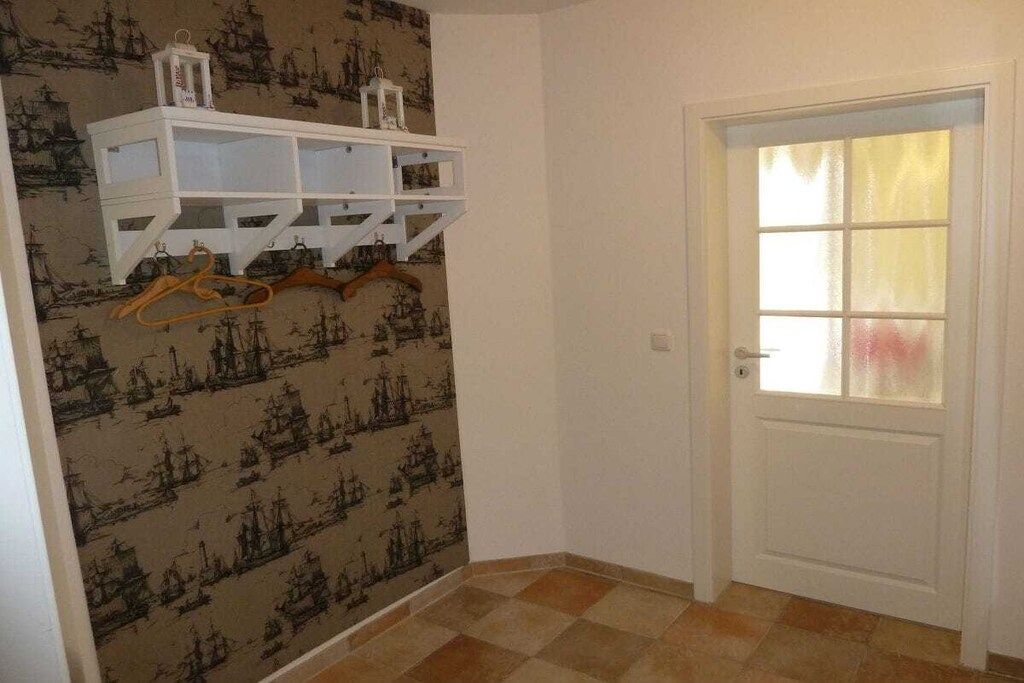 Une pièce avec un papier peint à motifs, une porte blanche dotée d’un panneau en verre dépoli et une étagère blanche pourvue de cintres.