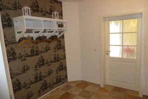 Una habitación con papel tapiz estampado, una puerta blanca con un panel de vidrio satinado y un armario blanco con perchas.