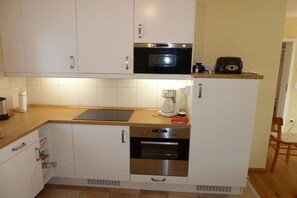 Cocina compacta con alacenas blancas, microondas, cafetera y tostadora sobre la encimera.