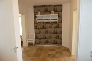 A room with a patterned wallpaper, a white chair, and a white shelf unit. - "The Yellow House 1" || Insel Poel OT Weitendorf (Insel Poel OT Weitendorf)