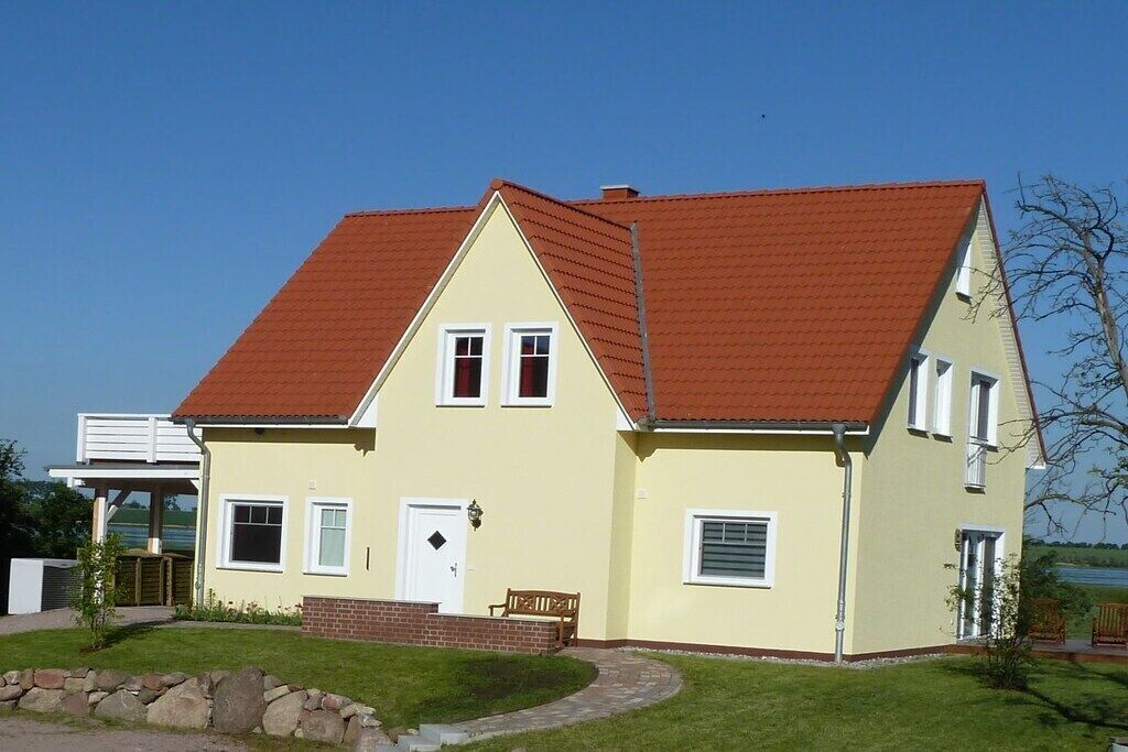 A two-story house with a red-tiled roof, a front porch, and a small garden area.