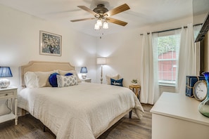A bedroom with a bed, bedside tables, a ceiling fan, a window with curtains, and a wall-mounted clock. - Explore Arlington! Centrally Located Extended Stay (Arlington)