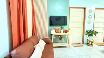 A living room with a brown sofa, a television, a wooden console table with decorative items, and a door with a mirror.