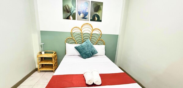 A hotel room with a bed, a small wooden side table, and a wall-mounted picture. - 2-bedroom Apartment Near City Center, Free WiFi & Parking (Puerto Princesa City)