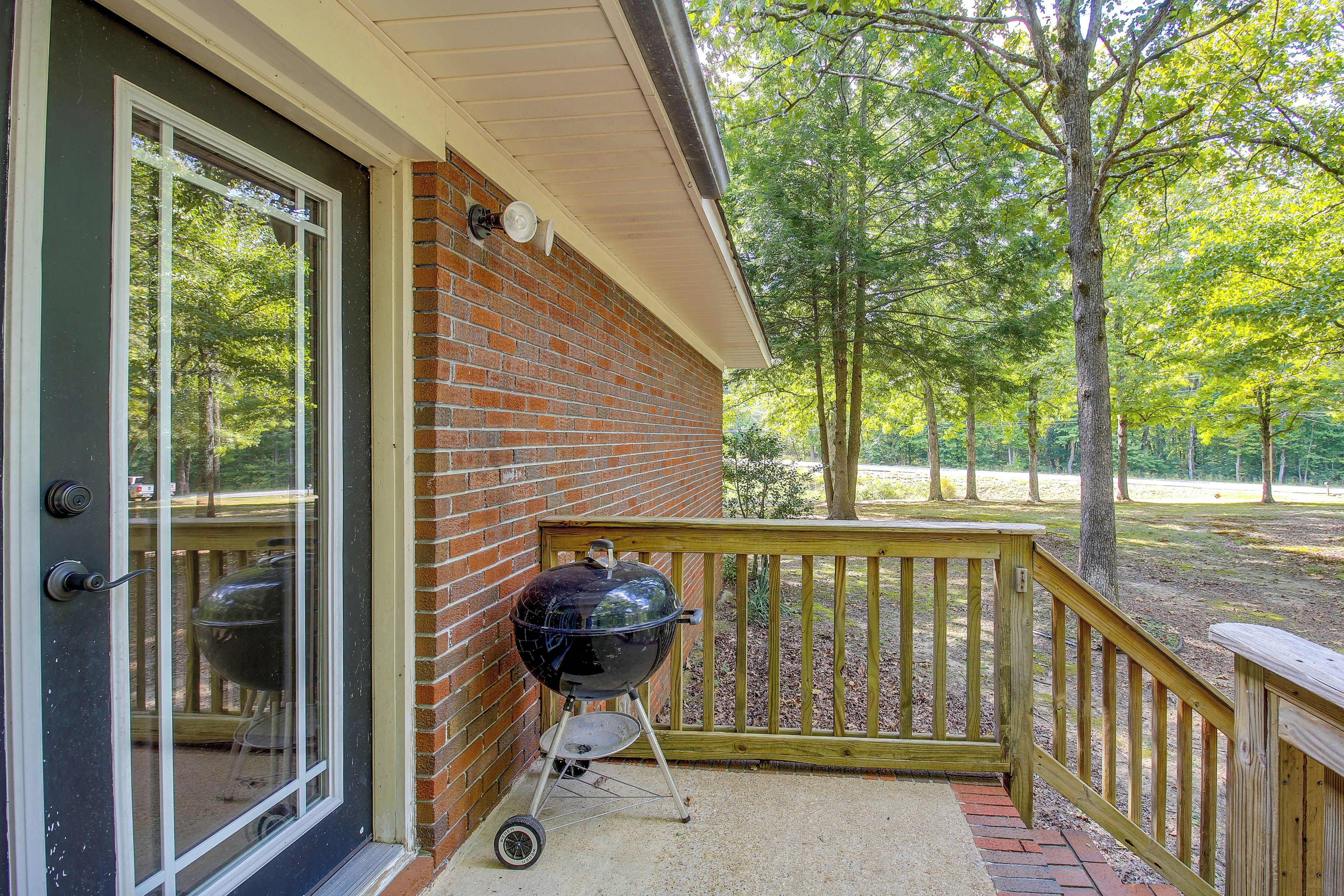 A brick exterior wall with a glass door, a wooden deck with a railing, and a barbecue grill.