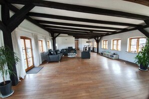 A spacious room with wooden flooring, a large sofa, a coffee table, and a TV. There are windows on the walls and a ceiling with exposed beams. - Above the Kattsund || Eckernförde (Eckernförde)
