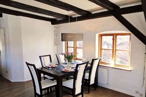 A dining area with a dark wooden table and chairs, a hanging light fixture, and a window with a view of buildings. - Above the Kattsund || Eckernförde (Eckernförde)