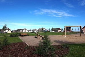 Ein Spielplatz mit Schaukel und Bank, umgeben von einer Rasenfläche und einem Weg.