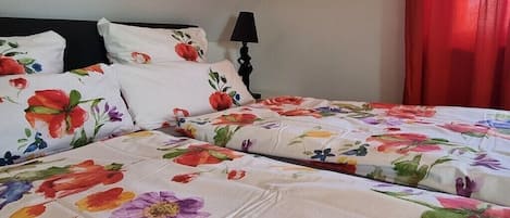 Un lit avec une literie à motifs floraux, une tête de lit noire, une lampe de chevet et un rideau rouge.