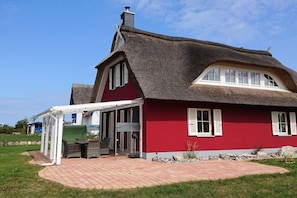 Ein rotes Haus mit einem Strohdach und einer überdachten Terrasse.