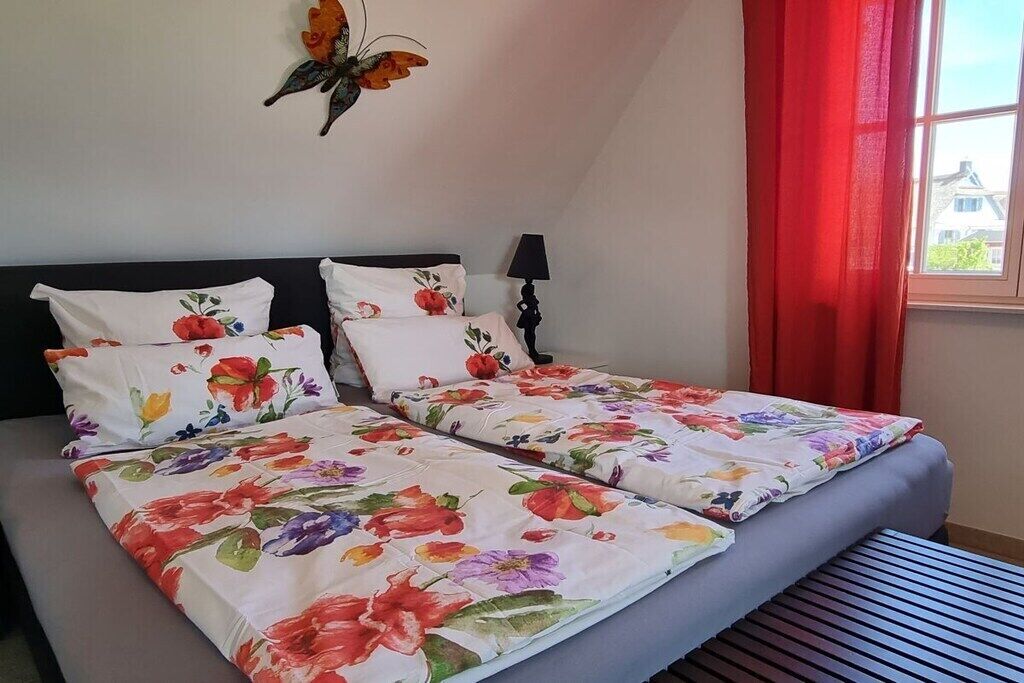 A double bed with floral bedding, a black headboard, a bedside lamp, and a window with red curtains.