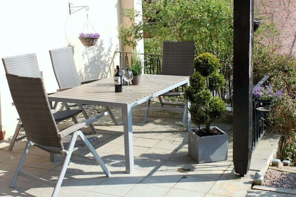 An outdoor patio with a table and chairs, a hanging plant, and a potted tree.