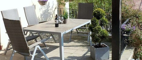 An outdoor patio with a table and chairs, a hanging plant, and a potted tree.